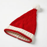 A red knitted Santa hat with a white ribbed cuff and fluffy white pompom lies diagonally on a white background.