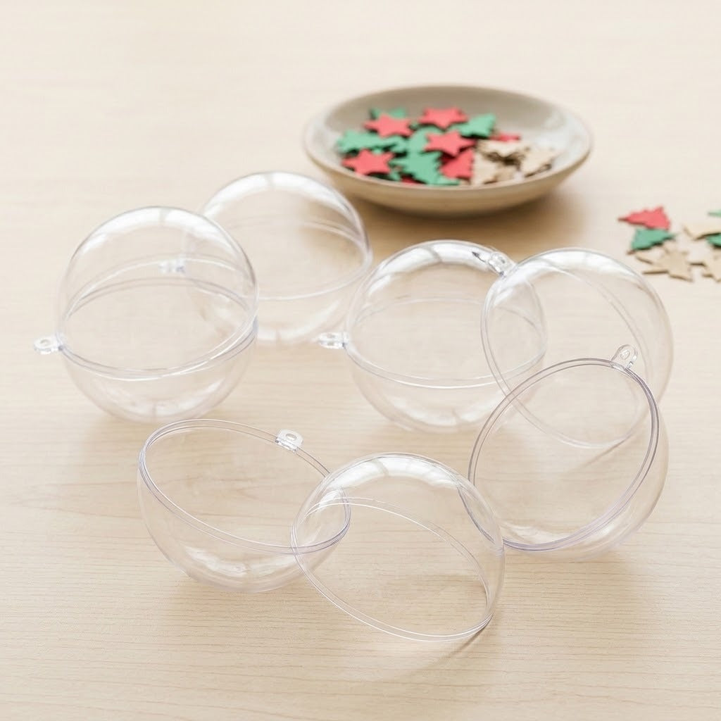 Clear plastic fillable ornaments lie open in halves on pale wood beside red, green, and beige craft shapes.