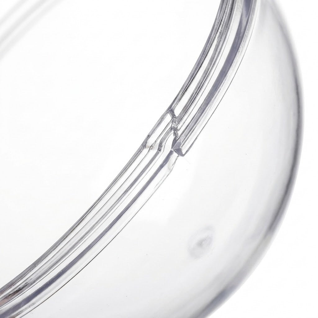 A clear plastic fillable ornament half appears close up, showing its curved joining rim against a white background.