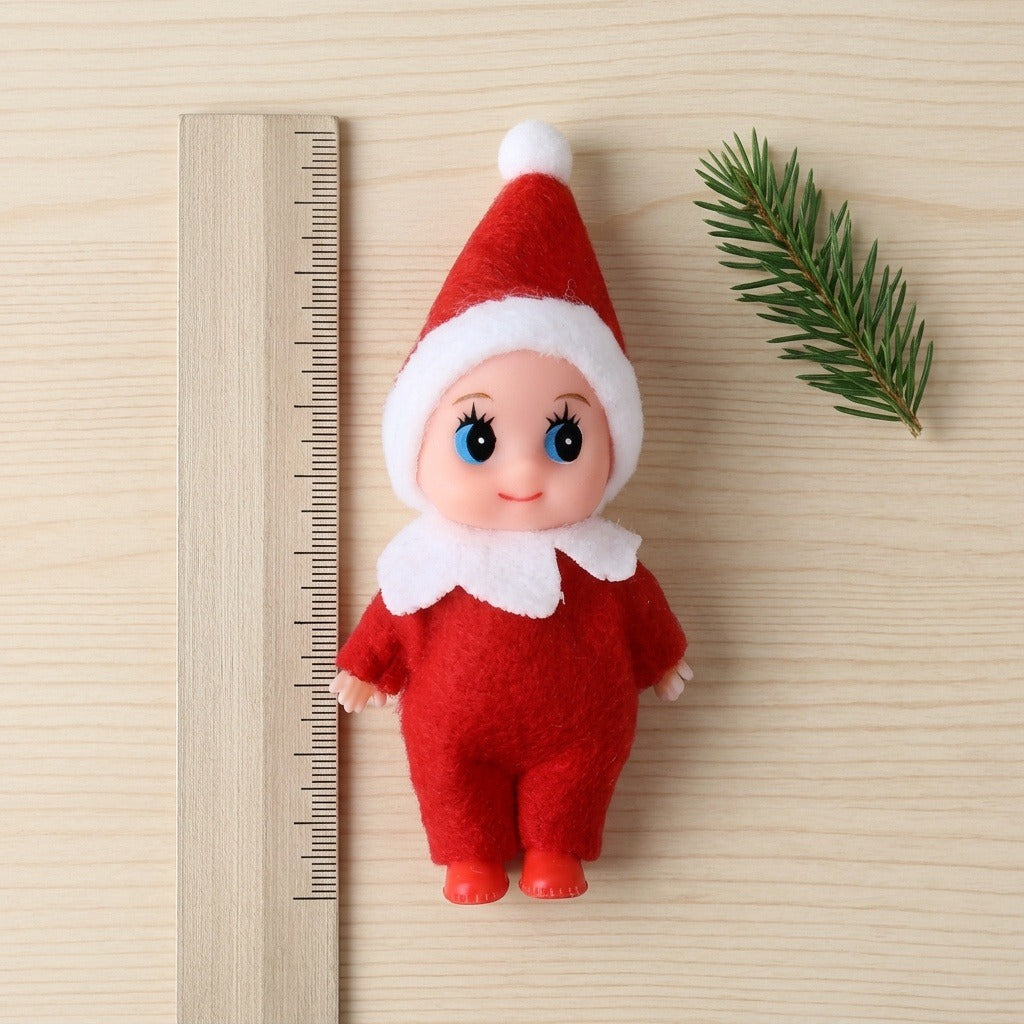 A red Christmas elf doll lies on pale wood beside a wooden ruler with unnumbered tick marks and an evergreen sprig.