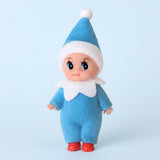 Elf doll wears a blue fabric outfit, white-trimmed pointed hat, white collar, and red shoes against a pale blue background.
