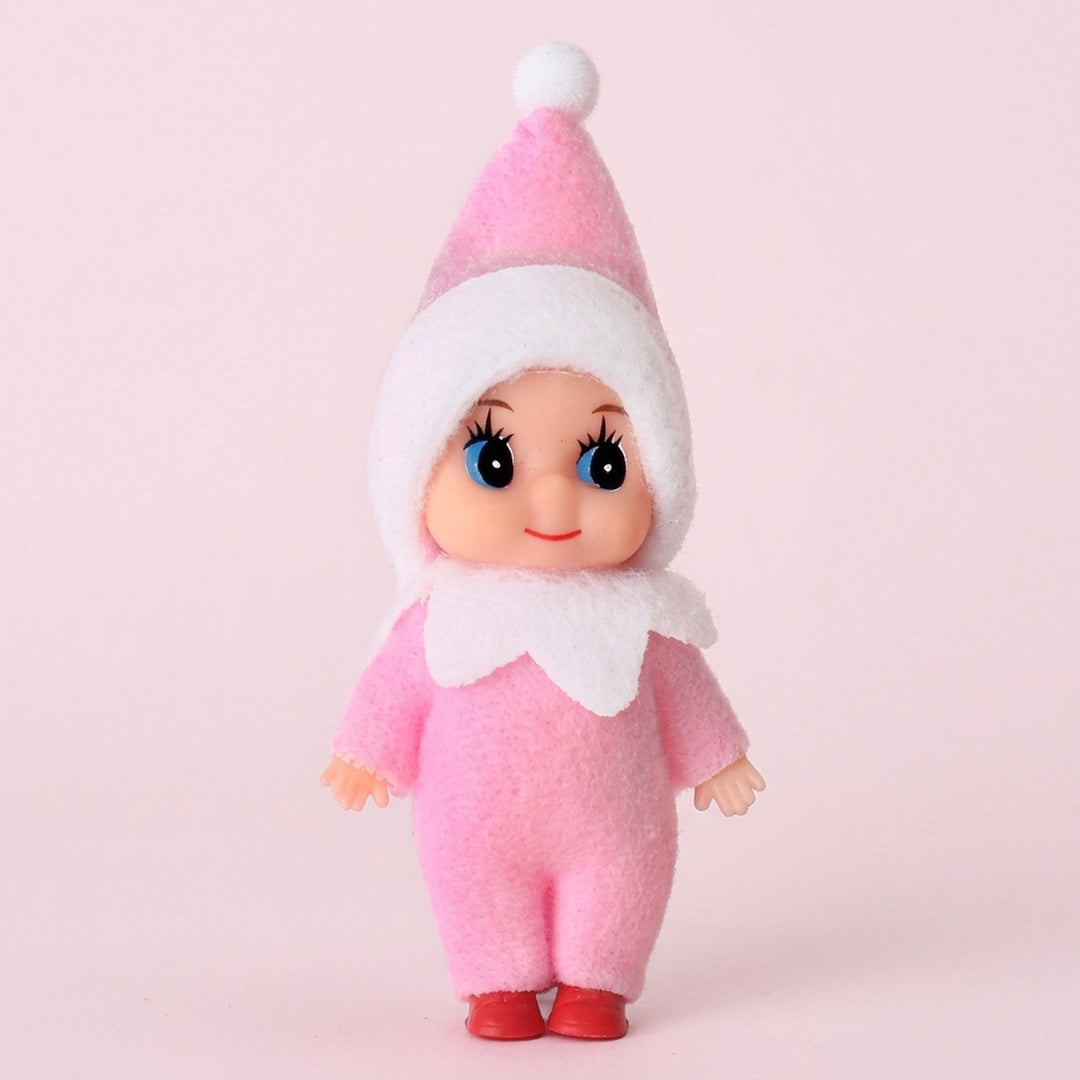 Elf doll wears a pink fabric outfit, white-trimmed pointed hat, white collar, and red shoes against a pale pink background.