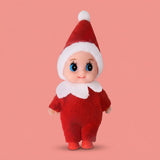 Elf doll wears a red fabric outfit, white-trimmed pointed hat, white collar, and red shoes against a coral background.