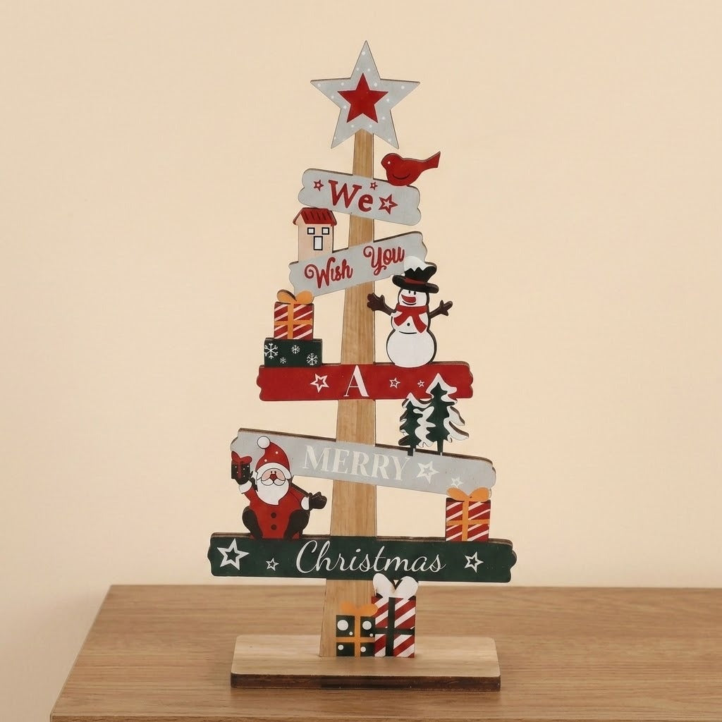 Wooden tabletop Christmas decoration with a white star topper, snowman and Santa cutouts stands on a wooden table against a beige wall.
