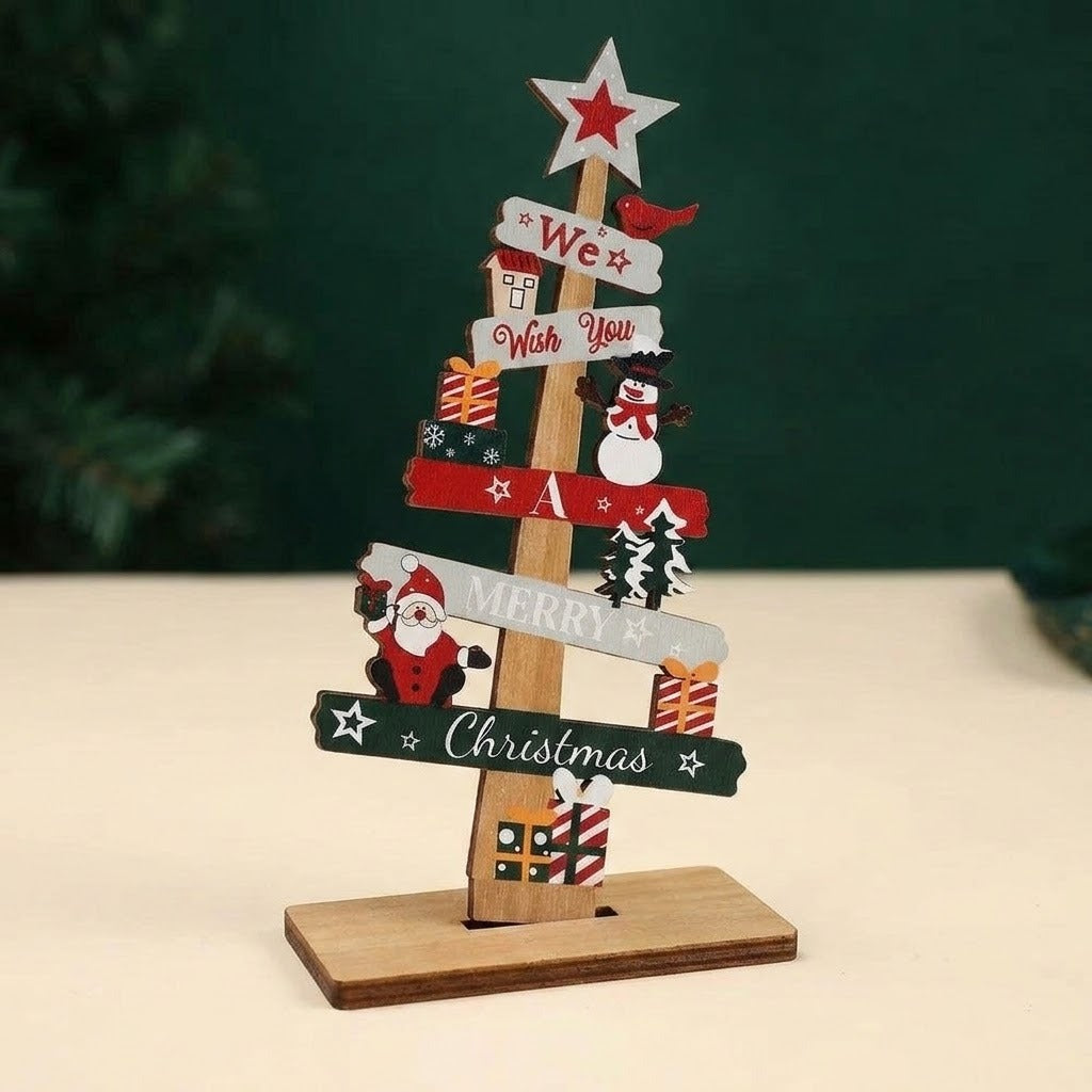 A wooden tabletop Christmas tree decoration with layered signs reading 'We Wish You a Merry Christmas,' decorated with red bird, snowman, Santa Claus, stars, and gift box illustrations, standing on a rectangular wooden base.