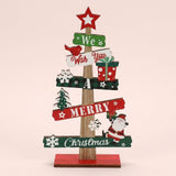 Wooden tabletop Christmas decoration with a red star topper, green and white signs, Santa and snowflakes stands against a pale pink background.