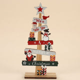 Wooden tabletop Christmas decoration features a white star with a red center, Santa, a snowman and presents against a beige background.