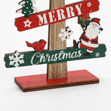 Wooden tabletop Christmas decoration close-up shows a red bird, Santa, white snowflakes and green Christmas slat above a red base against white.