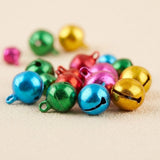 Close-up of multicoloured metallic jingle bells showing hanging loops and curved openings on a beige surface.