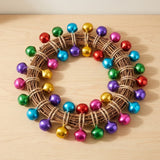 Multicoloured shiny jingle bells are tied with twine around a brown twig wreath lying on a light wooden tabletop.