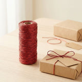 Metallic red craft cord stands on a spool beside a kraft gift box tied with matching cord on a light wood table.