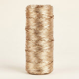 Champagne gold craft cord with a metallic sheen is wound on an upright spool against a cream background.