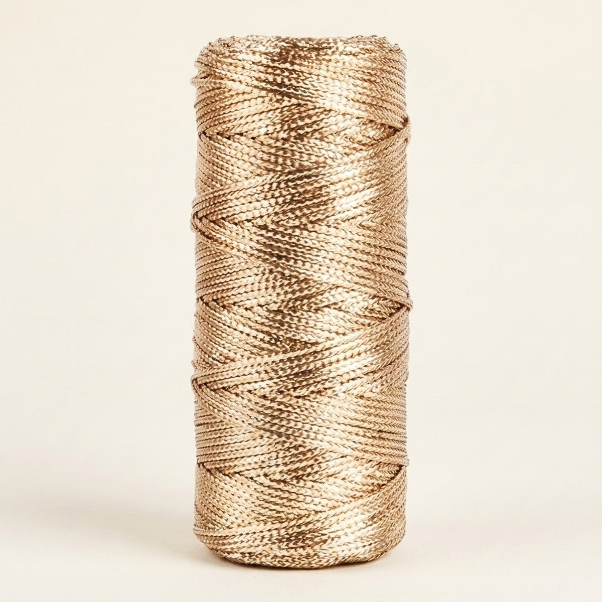 Champagne gold craft cord with a metallic sheen is wound on an upright spool against a cream background.
