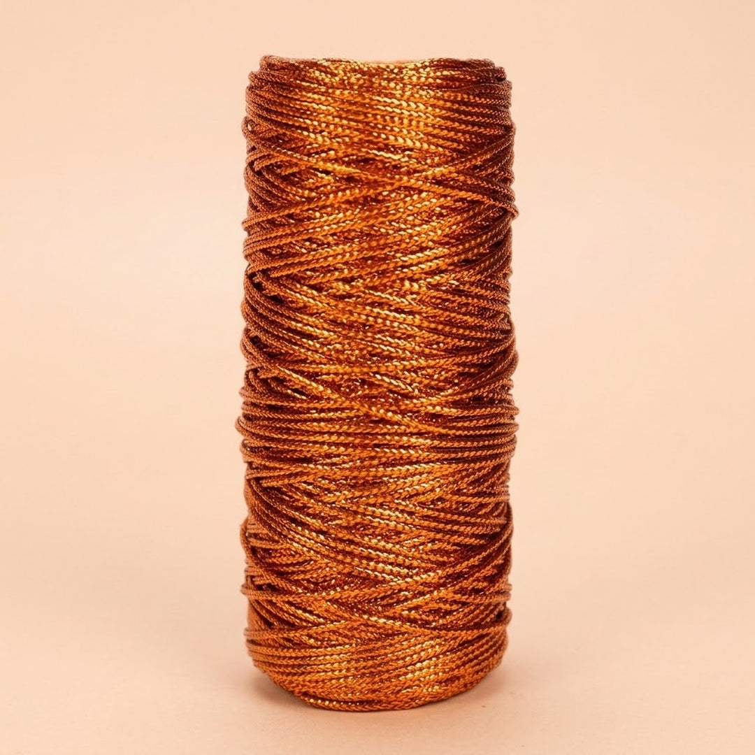 Copper-coloured craft cord with a metallic sheen is wound in overlapping strands on an upright spool against a pale peach background.