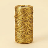 A gold metallic craft cord spool stands upright against a pale yellow background, showing overlapping strands and a visible central opening.