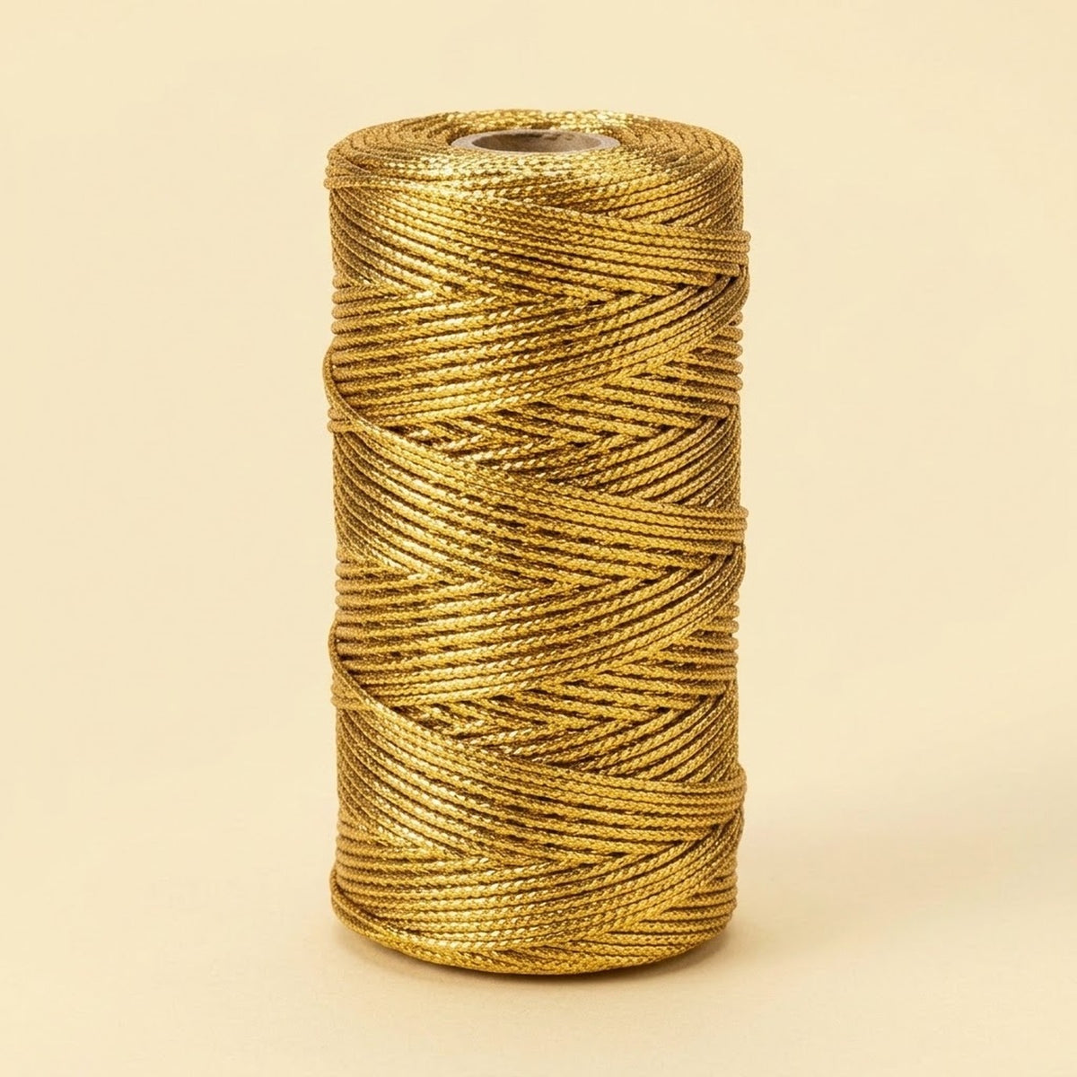 A gold metallic craft cord spool stands upright against a pale yellow background, showing overlapping strands and a visible central opening.