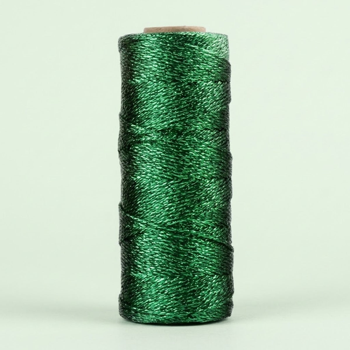 Shiny green twisted craft cord is wound around an upright cardboard spool against a pale green background.