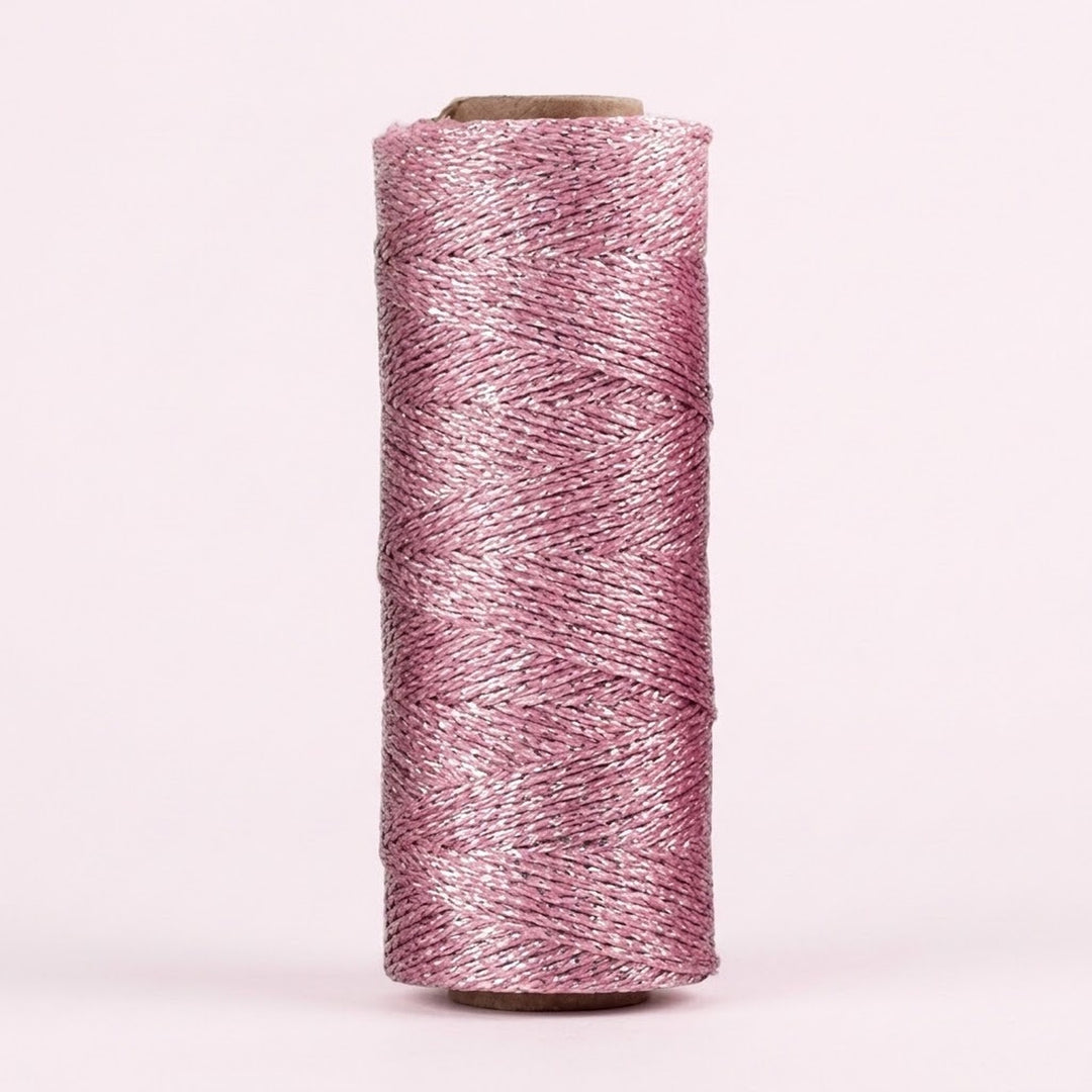 Shiny light pink twisted craft cord is wound around an upright cardboard spool against a pale pink background.
