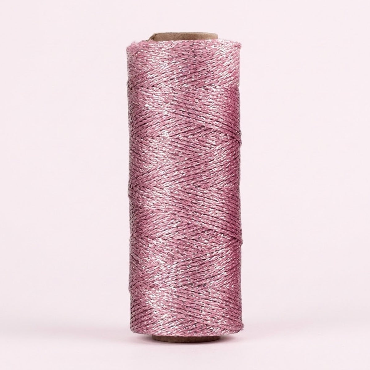 Shiny light pink twisted craft cord is wound around an upright cardboard spool against a pale pink background.
