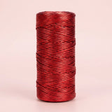 Shiny red craft cord is wound in overlapping strands on an upright spool against a pale pink background.