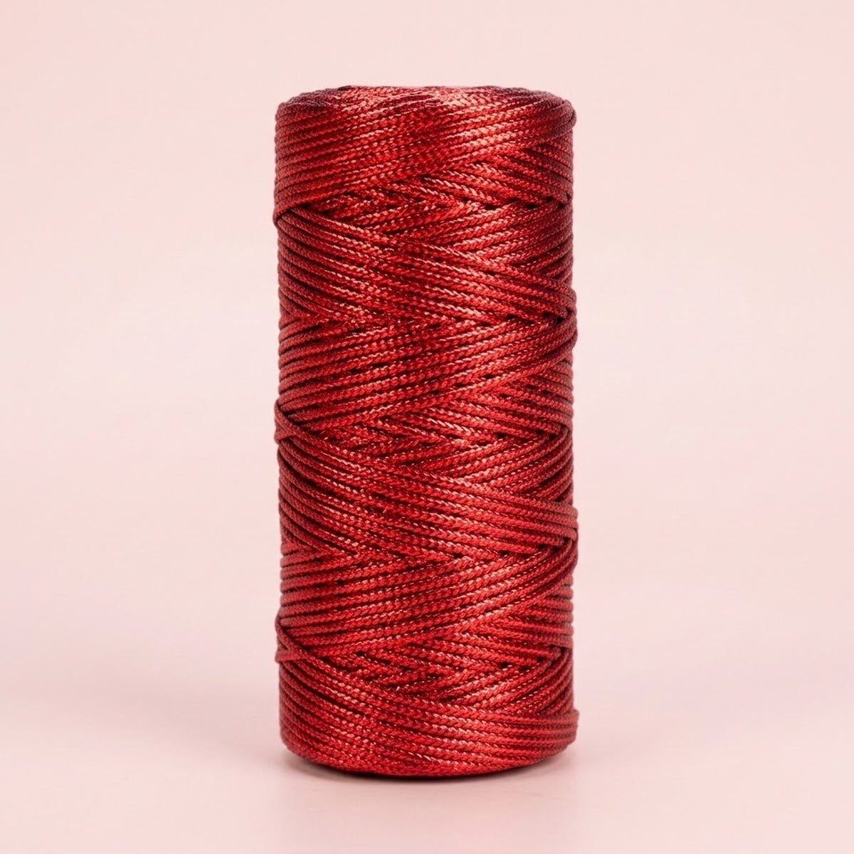 Shiny red craft cord is wound in overlapping strands on an upright spool against a pale pink background.