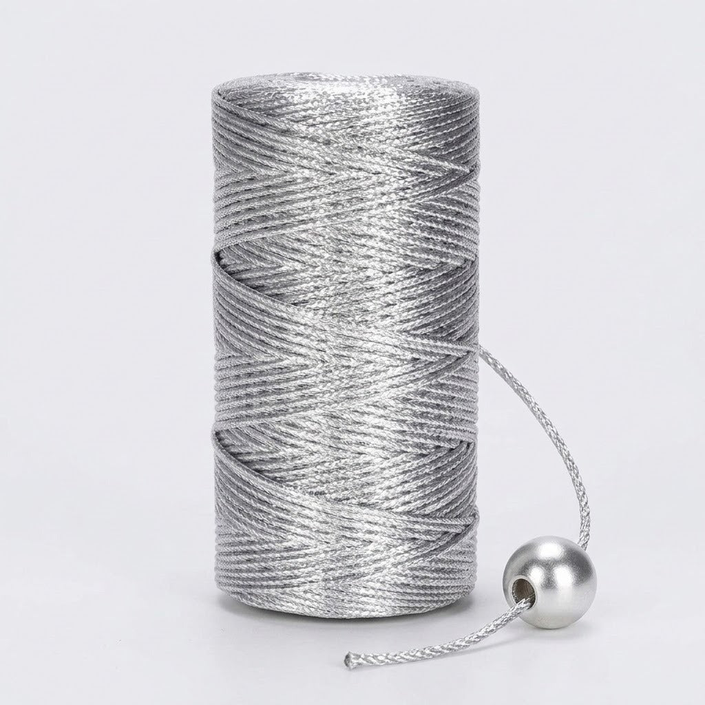 A silver metallic craft cord spool stands on a light grey background with its loose end threaded through a round silver bead.