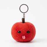 A red plush apple keychain with black eyes, a pink tongue, brown stem, and silver ring stands against a white background.