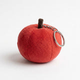 The back of a red plush apple keychain shows curved seams, a brown stem, and a silver ring against a white background.
