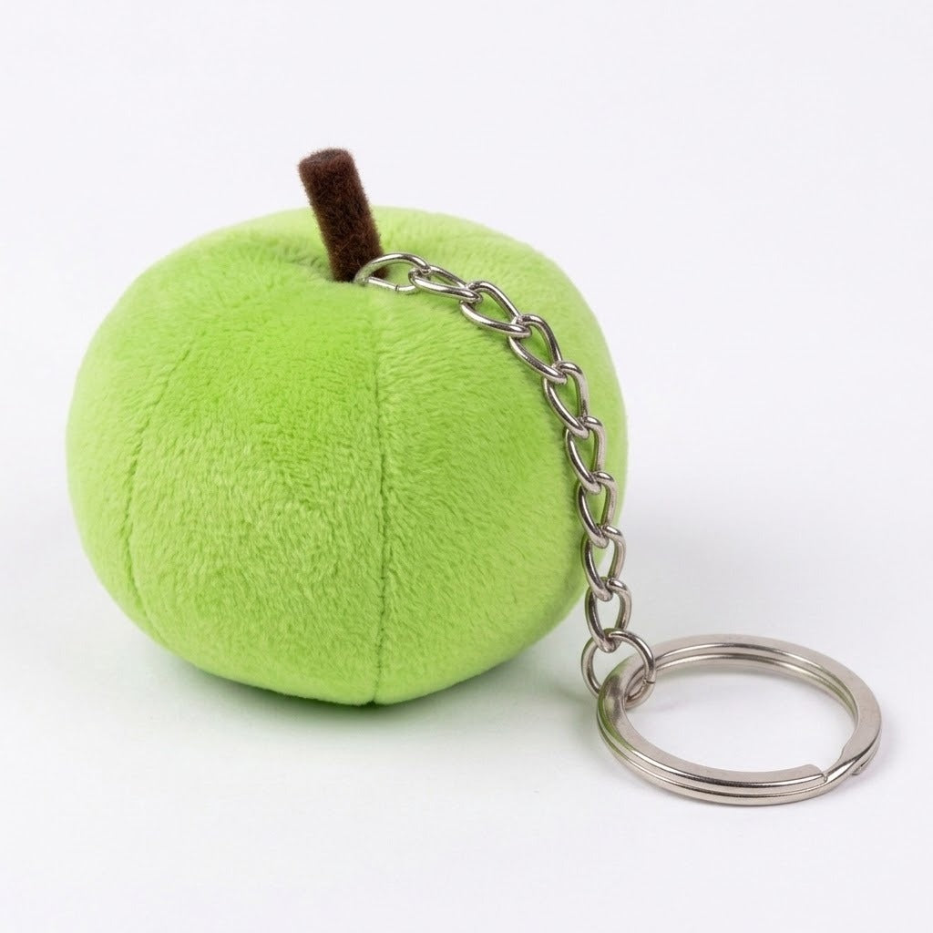 A green plush apple keychain viewed from behind has stitched seams, a brown stem, and a silver chain extending across a white surface.