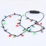 A light-up necklace with unlit multicoloured bulbs, black twisted wire and a rectangular black battery box lies loosely looped on white.