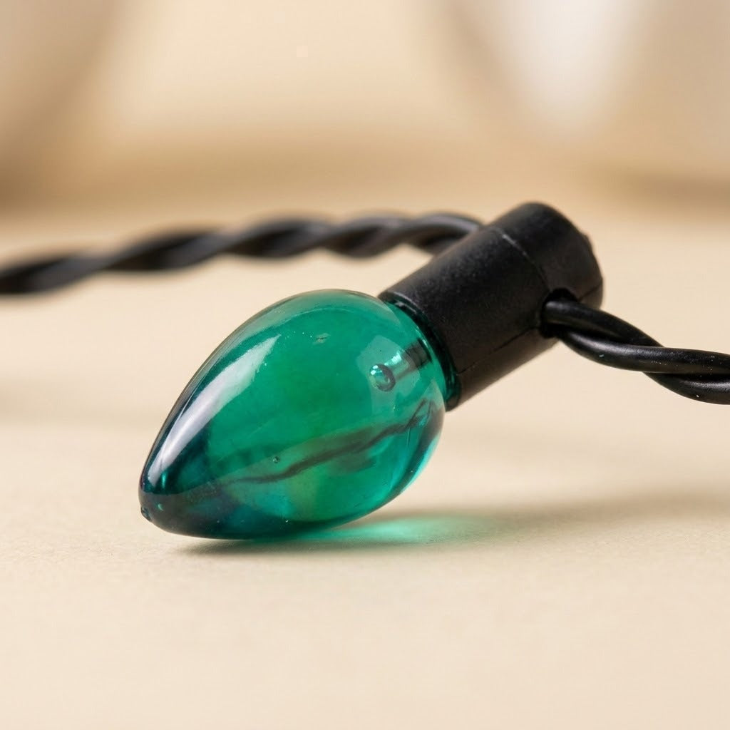 A close-up shows the light-up necklace’s translucent green plastic bulb, black socket and twisted black wire against a beige background.