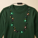 A light-up necklace with multicoloured plastic bulbs and a black battery box drapes over a dark green sweater.