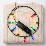 A light-up necklace with glowing multicoloured bulbs loops around its black battery box on a folded cream cable-knit sweater.