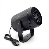 Black snowflake projector with a perforated circular front, U-shaped support bracket, and coiled USB cable against a white background.