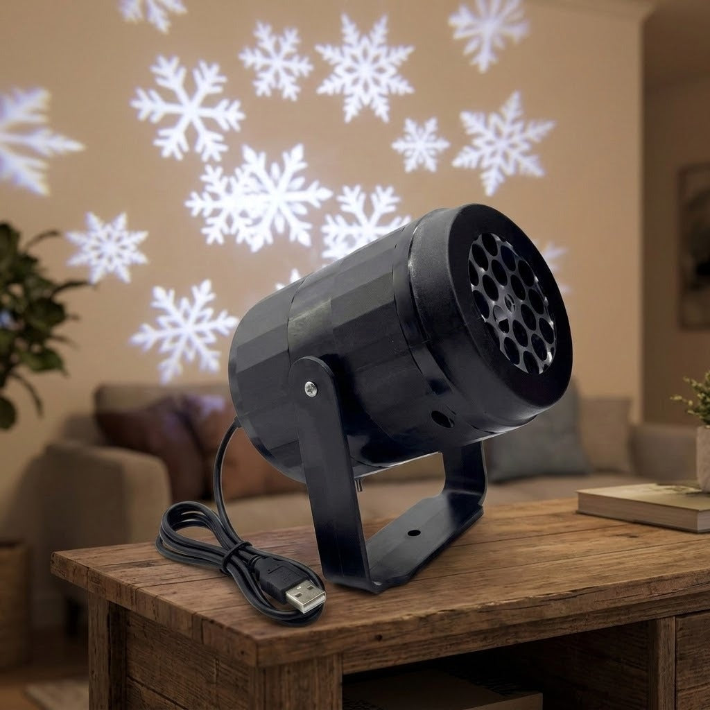 Black projector with coiled USB cable stands on a wooden coffee table, with white snowflakes projected above a sofa.