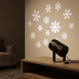 Rear view of a black projector on a wooden console shows its tilted stand and USB cable beneath white snowflake projections.