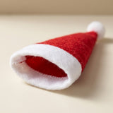 A red fabric Santa hat cutlery holder rests on a beige surface, showing its white trimmed opening, interior stitching, and white pompom.