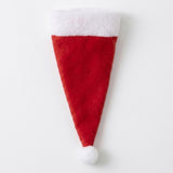 A single red fabric Santa hat cutlery holder with a broad white cuff and white pompom lies flat on a white background.
