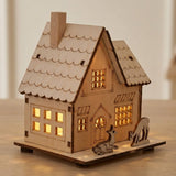 A pale wooden Christmas house with two deer figures glows through cutout windows on a wooden tabletop against a cream wall.