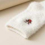 White fuzzy sock with a ribbed cuff and small brown embroidered motif with a red detail rests on a beige surface.