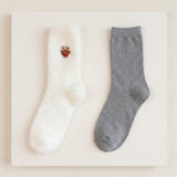 Two crew socks displayed side by side on a white rectangular board. The left sock is white with a small embroidered reindeer motif near the cuff.