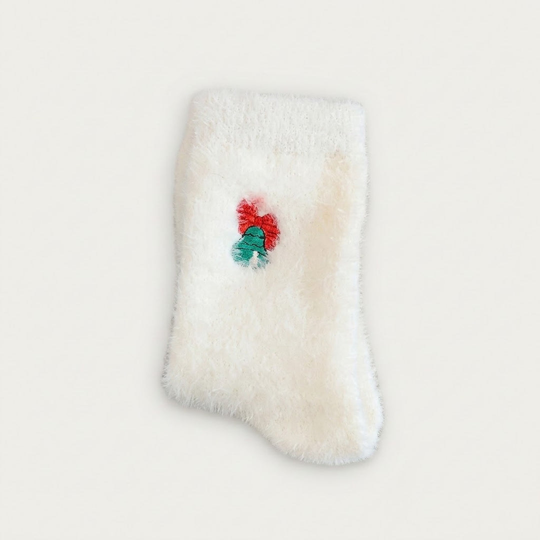 A fluffy white sock with green bells and a red bow lies flat on a pale background.