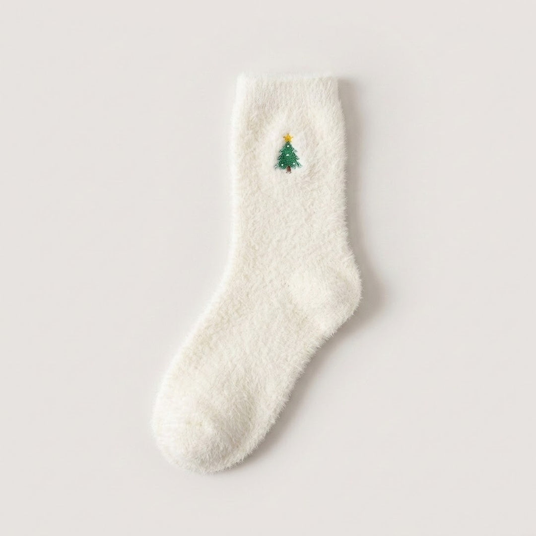 A fluffy white sock with a green Christmas tree and yellow star lies flat on a pale background.