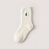 A fluffy white sock with a green Christmas tree and yellow star lies flat on a pale background.