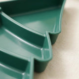 A close-up of the dark green serving tray shows its smooth surface, raised rim, and curved divider on a beige background.