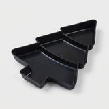 Black Christmas tree serving tray with three divided compartments sits diagonally against a light grey background.
