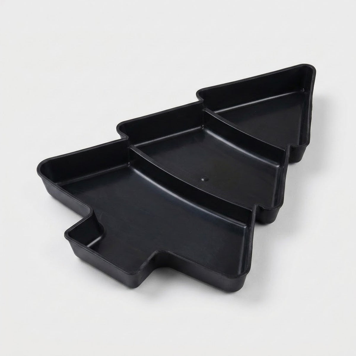 Black Christmas tree serving tray with three divided compartments sits diagonally against a light grey background.