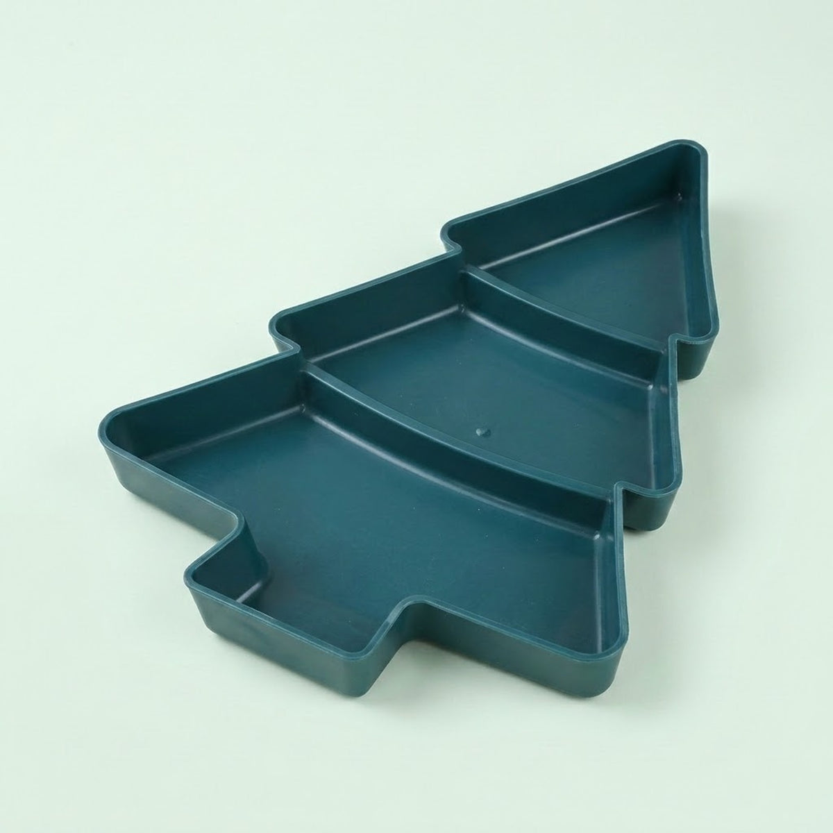 Dark green Christmas tree serving tray with three divided compartments sits diagonally against a pale green background.