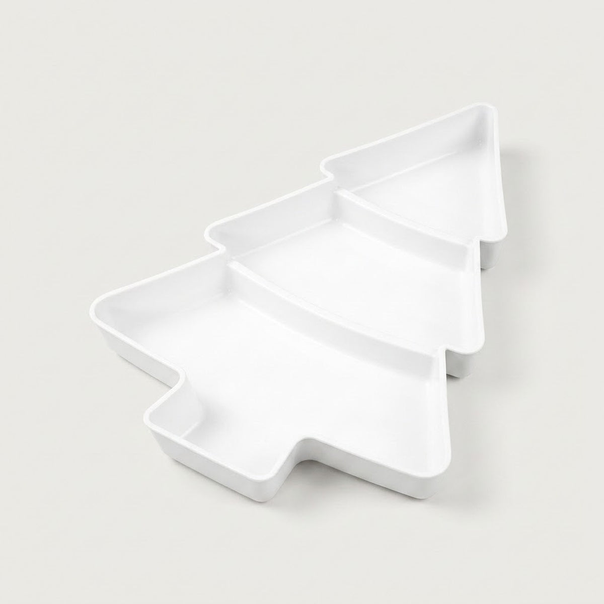 White Christmas tree serving tray with three divided compartments sits diagonally against an off-white background.