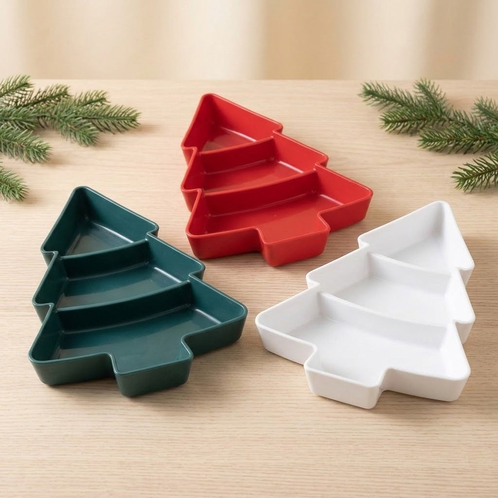 Dark green, red, and white Christmas tree serving trays each have three empty compartments and sit on a wooden tabletop among evergreen sprigs.